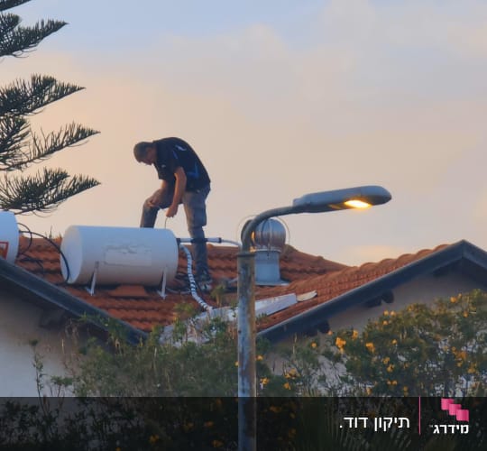 אדם עובד על דוד שמש על גג רעפים